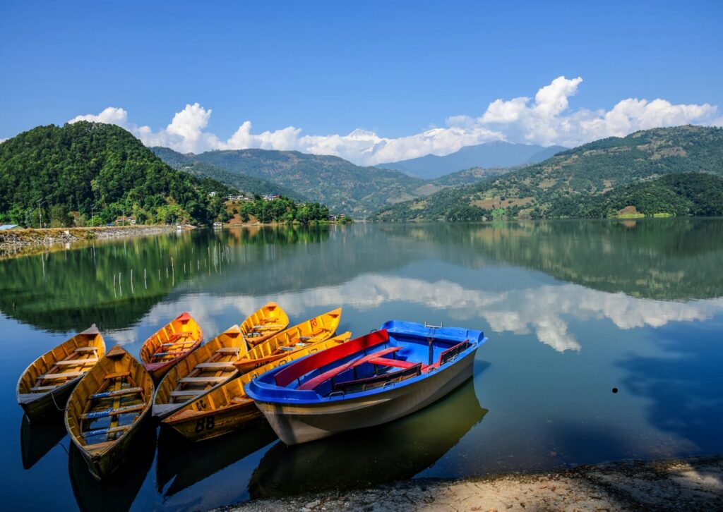 Three boats are moored on the edge of a tranquil lake, with trees lining the shore.
