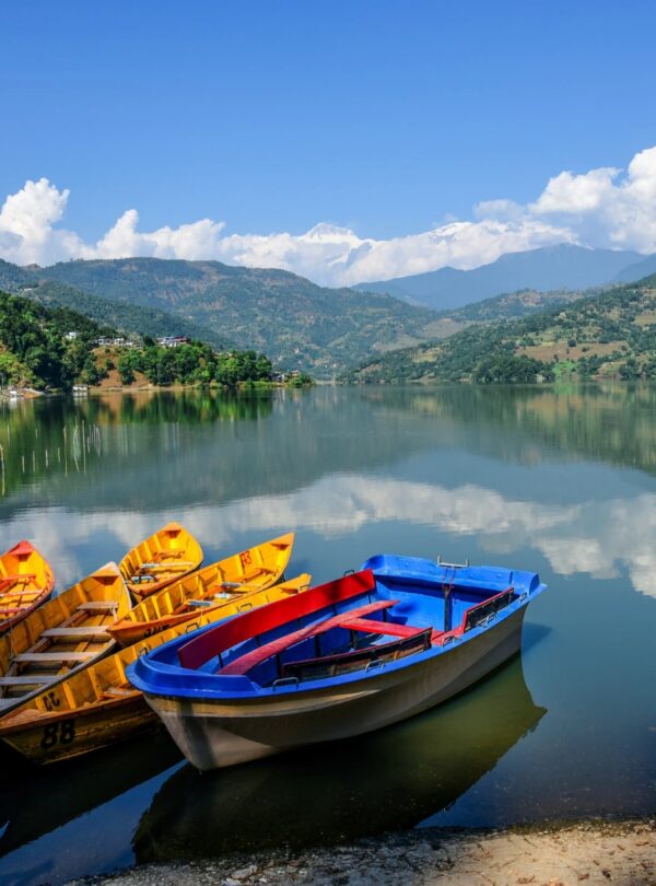 Three boats are moored on the edge of a tranquil lake, with trees lining the shore.