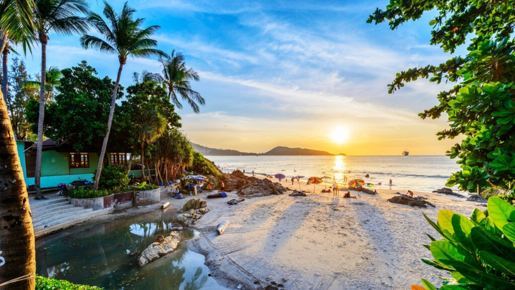 A serene beach in Thailand at sunset, with vibrant orange and pink hues reflecting on the calm water.